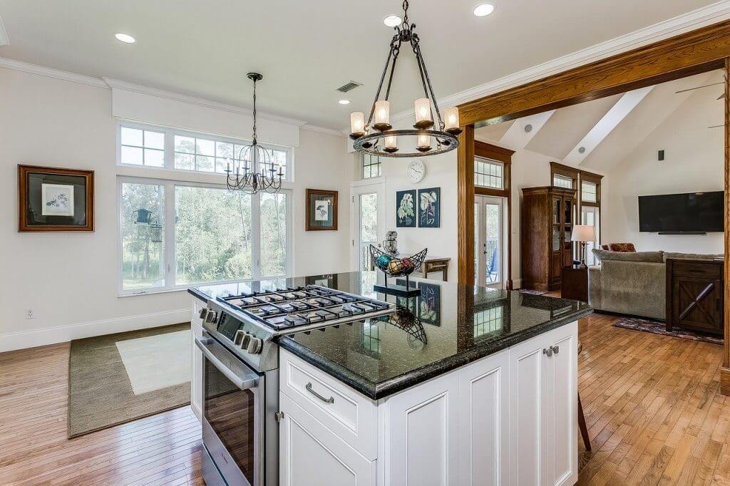 Kitchen remodeled with island top range stove, white wood cabinet, pedant light and hard wood flooring in neighbor home