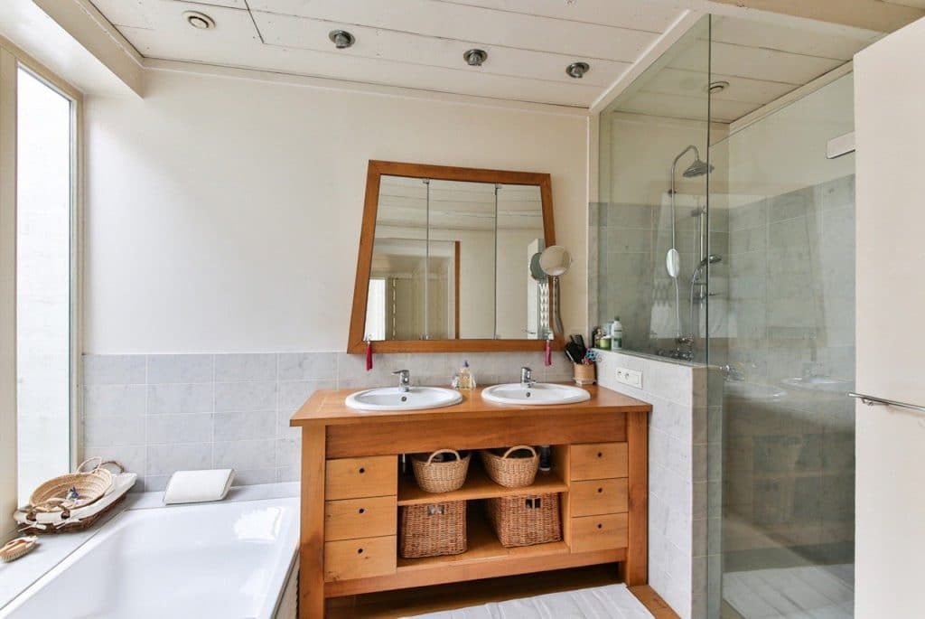A newly home bathroom remolded with pine basin cabinet, white ceramic bath tub, glass shower screen and a medium size mirror with some elements